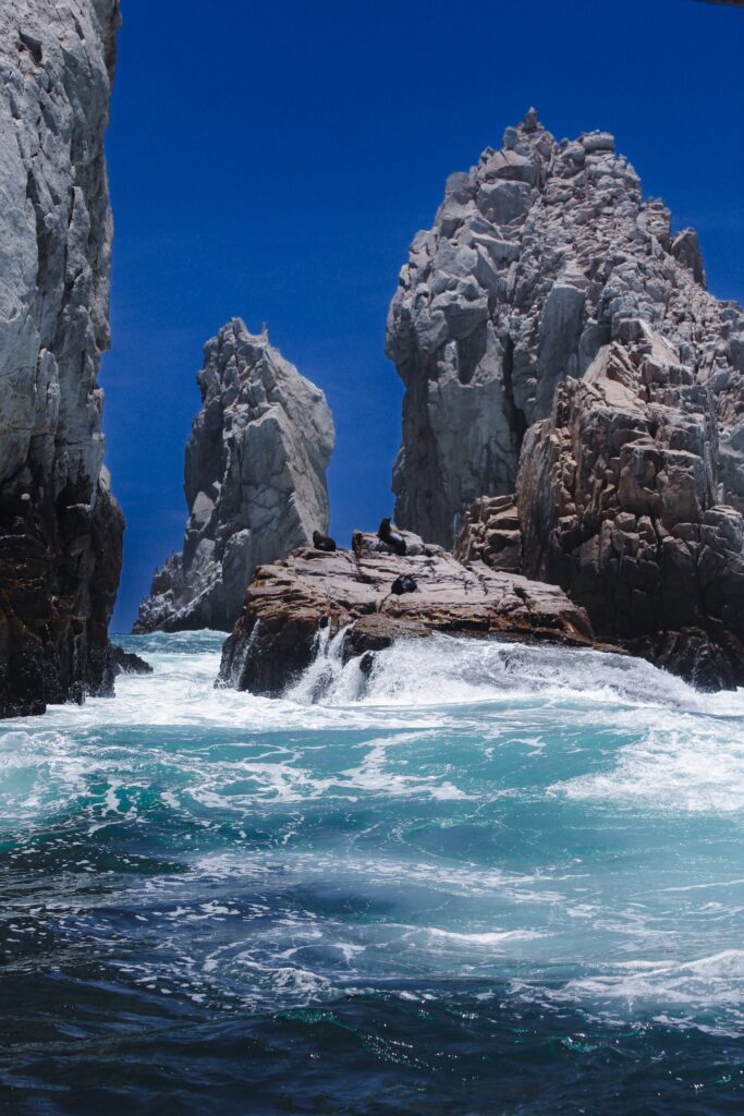 Glass Bottom Boat Dramatic rock formations and sea waves at Cabo San Lucas under a clear blue sky.